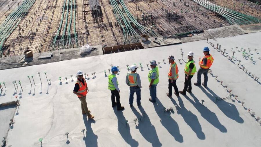 Aerial view of construction workers in safety gear having a meeting on a concrete foundation with rebar framework in the background